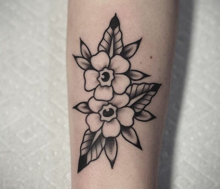 American traditional tattoo design featuring two black and white flowers with leaves on an arm.