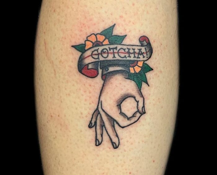 American traditional tattoo with a hand gesture, floral accents, and "Gotcha" banner.