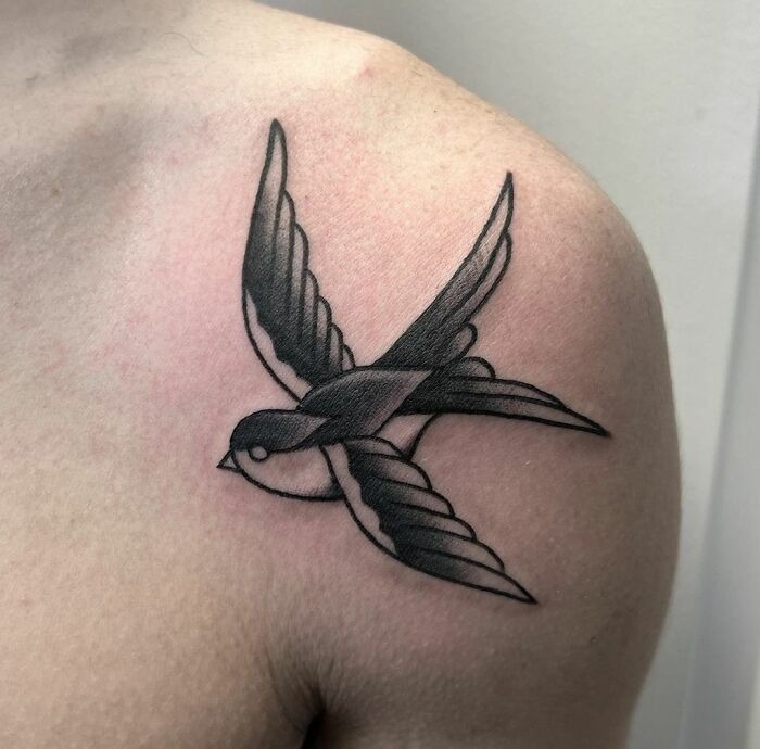 American traditional tattoo of a swallow on shoulder, showcasing bold lines and classic design elements.