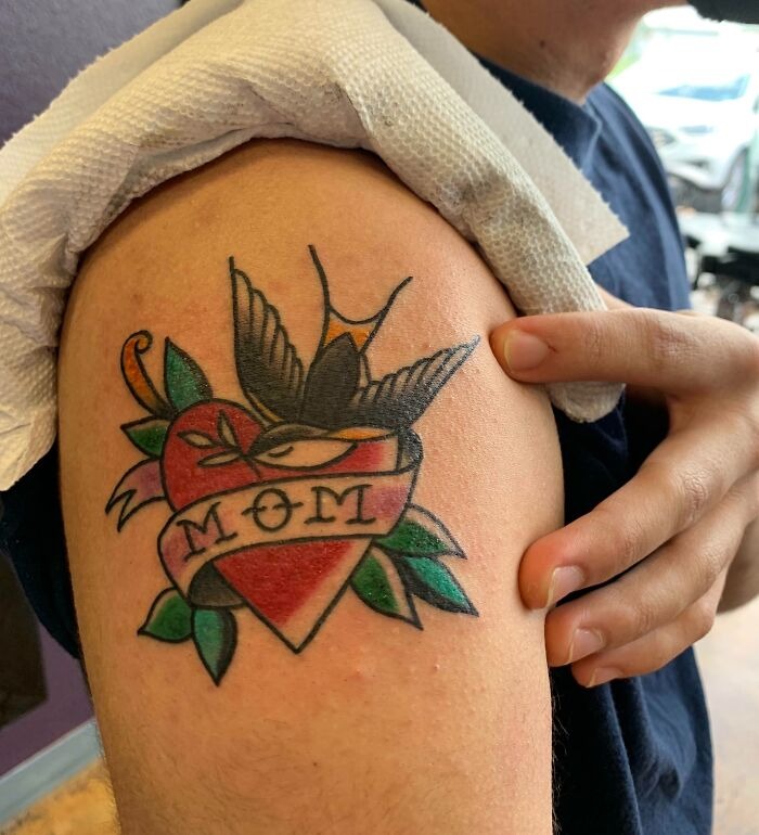 American traditional tattoo of a heart with the word "Mom" and a swallow on the upper arm.