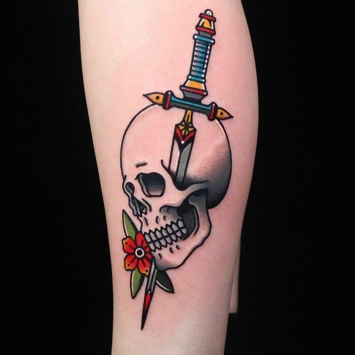 American traditional tattoo featuring a skull with a dagger and a red flower on an arm.