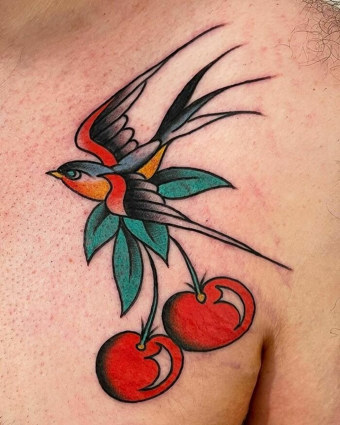 American traditional tattoo of a bird with cherries on male chest, featuring bold colors and classic design elements.