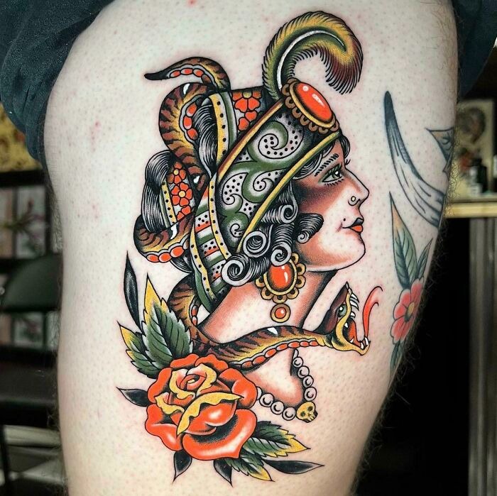 American traditional tattoo featuring an ornate g***y woman with feathers and flowers, showcasing classic bold colors and patterns.