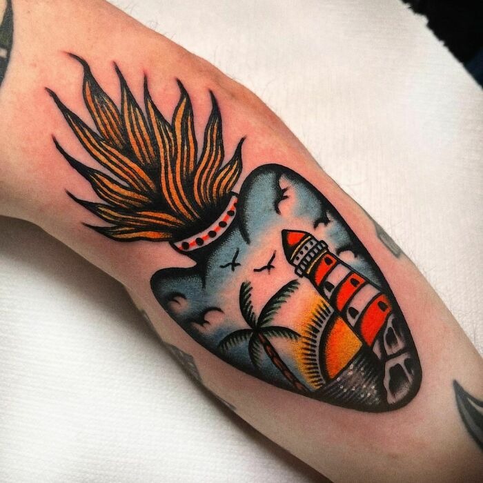 American traditional tattoo featuring a lighthouse, palm tree, and sunset flame on an arm.
