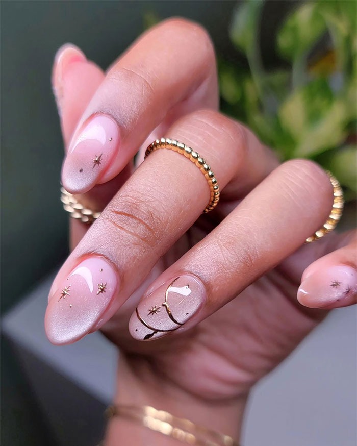 Close-up of almond nails with soft pink polish and delicate gold star accents, showcasing popular almond nails trends.