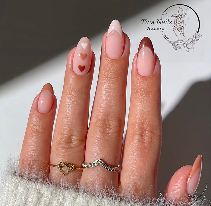 Hand with glossy almond nails in soft pink shades and heart designs, showcasing popular almond nails trends for 2025.