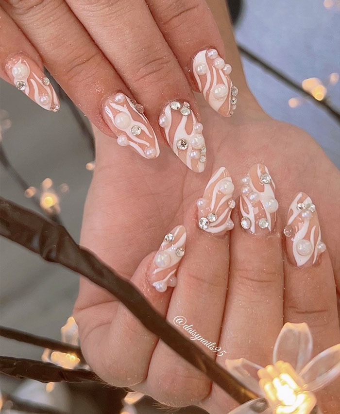 Almond nails with white swirl designs adorned with pearls and rhinestones, showcasing top almond nails trends for 2025.