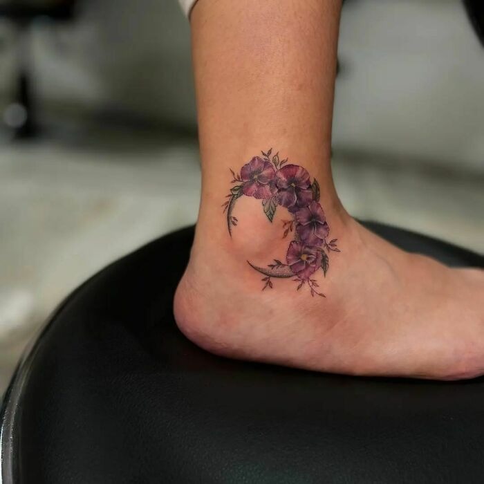 Floral ankle tattoo with purple flowers, creating a crescent shape, showcasing beautiful flower tattoos on skin.