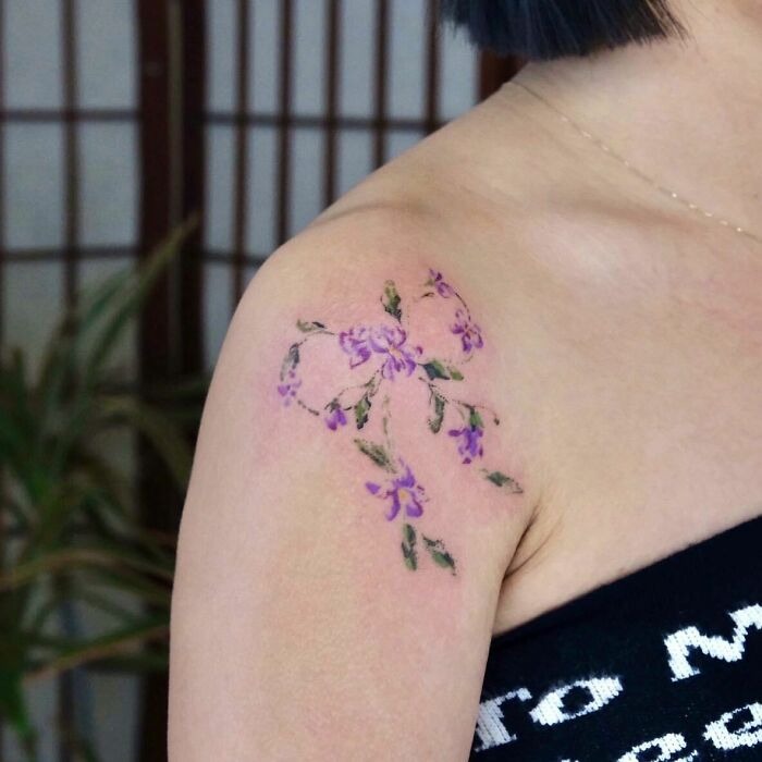 Purple flower tattoo on shoulder, delicate and vibrant, resembling real blossoms against the skin.