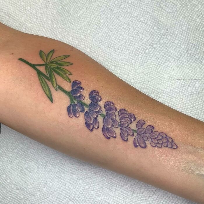 Purple flower tattoo on forearm, illustrating delicate floral design blossoming on the skin.