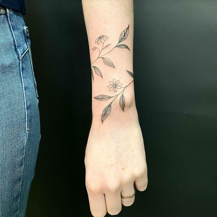 Flower tattoo with delicate blossoms and leaves on forearm, resembling natural growth on the skin.