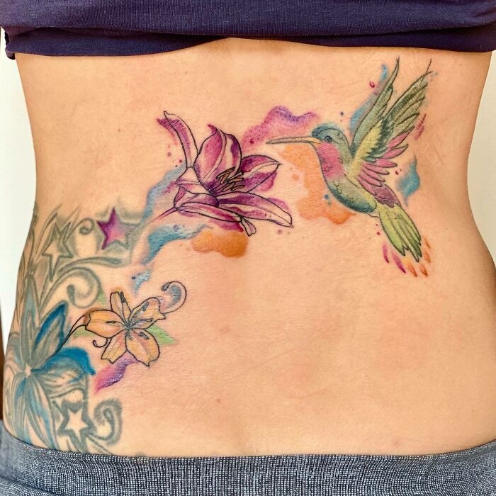 Flower tattoo with a hummingbird on skin, featuring colorful blossoms and intricate designs.