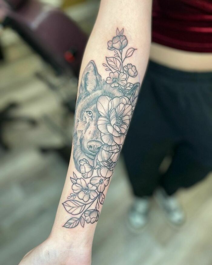 Intricate flower tattoos with a wolf design on forearm, appearing to blossom on the skin.