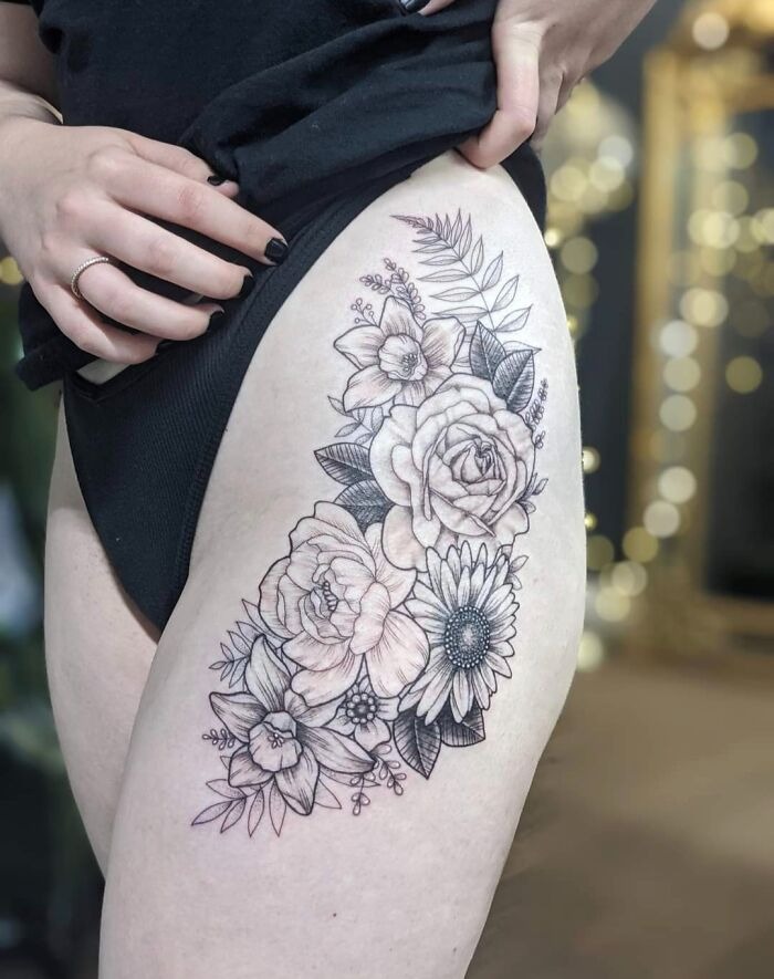 A detailed flower tattoo on a thigh showcasing roses and leaves.