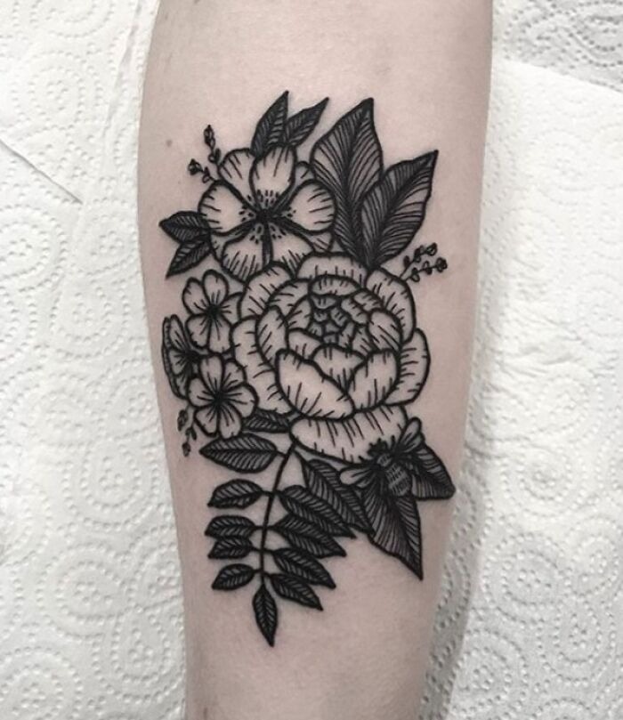 Black ink flower tattoo design on forearm, featuring blooming blossoms and detailed leaves.