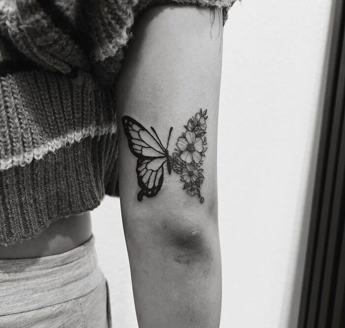 Butterfly and flower tattoo design on arm showcasing intricate linework and shading.