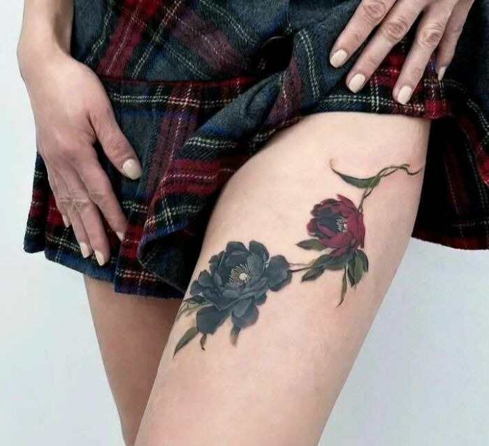 Person showing thigh with vibrant flower tattoos under a plaid skirt.