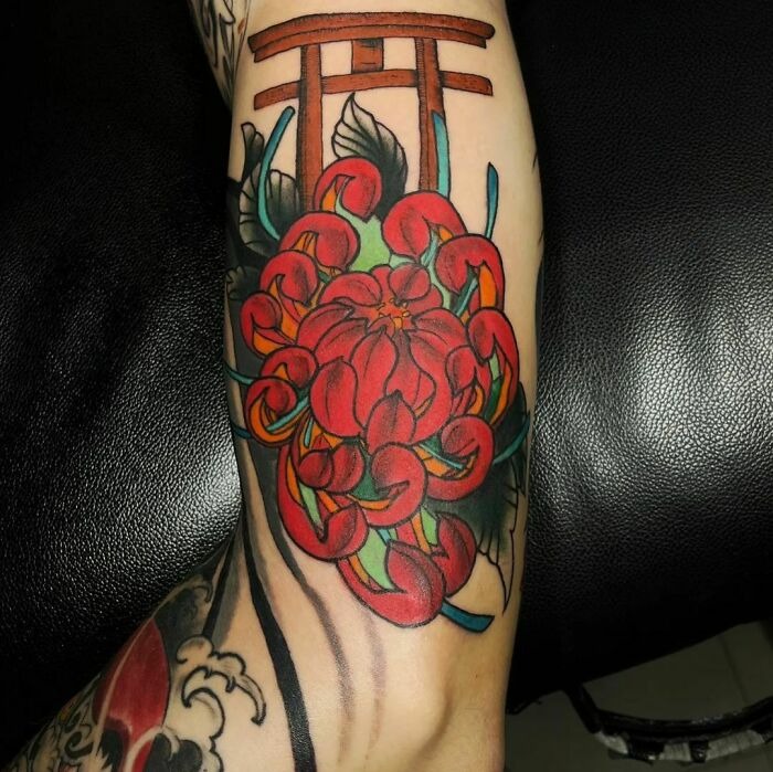Red flower tattoo on forearm, vibrant petals intertwining with Japanese torii gate design.