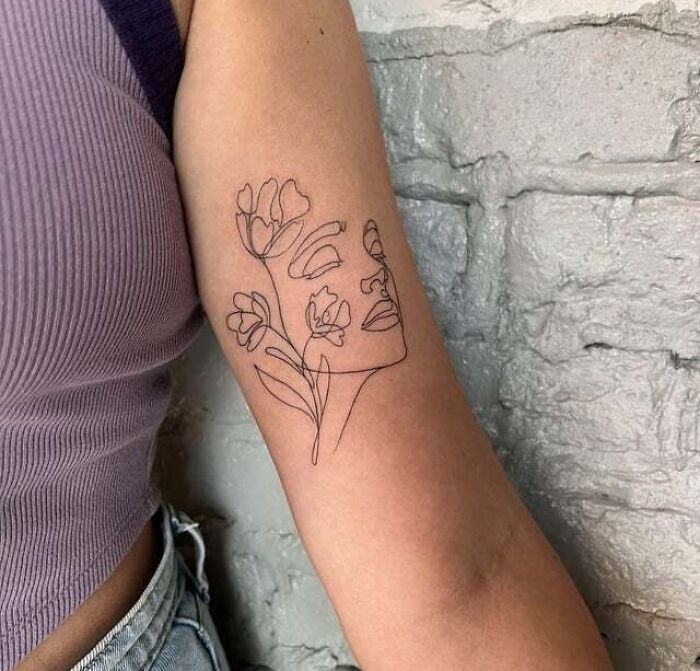Line art flower tattoo with a face on an arm, seamless blend on skin.
