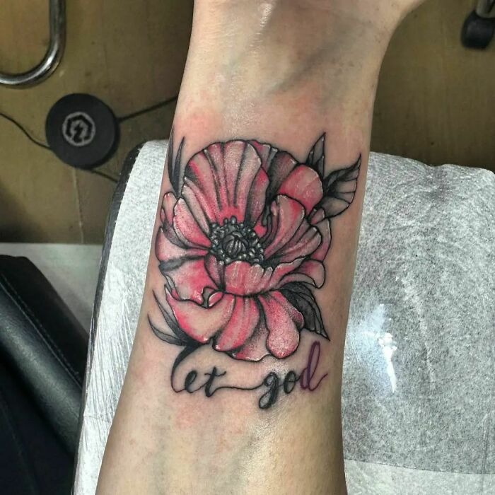 Pink flower tattoo with black leaves and the phrase "let go" on forearm, showcasing vibrant blossom design.